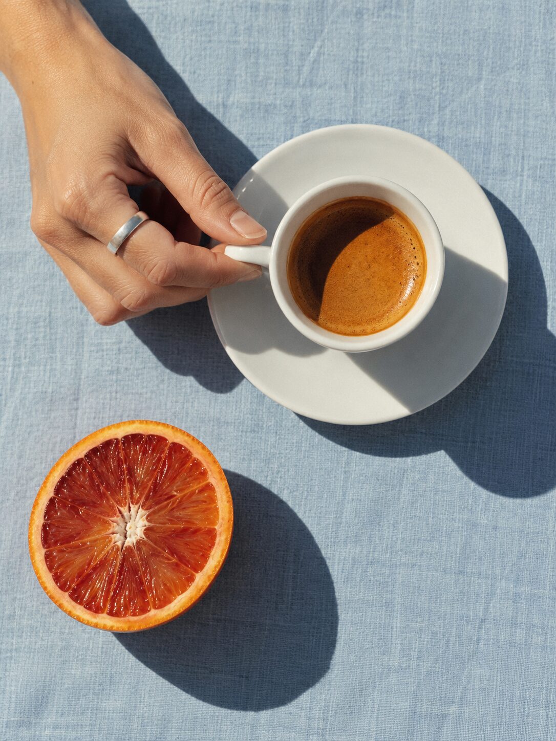 Hand mit Espressotasse neben einer Blutorange