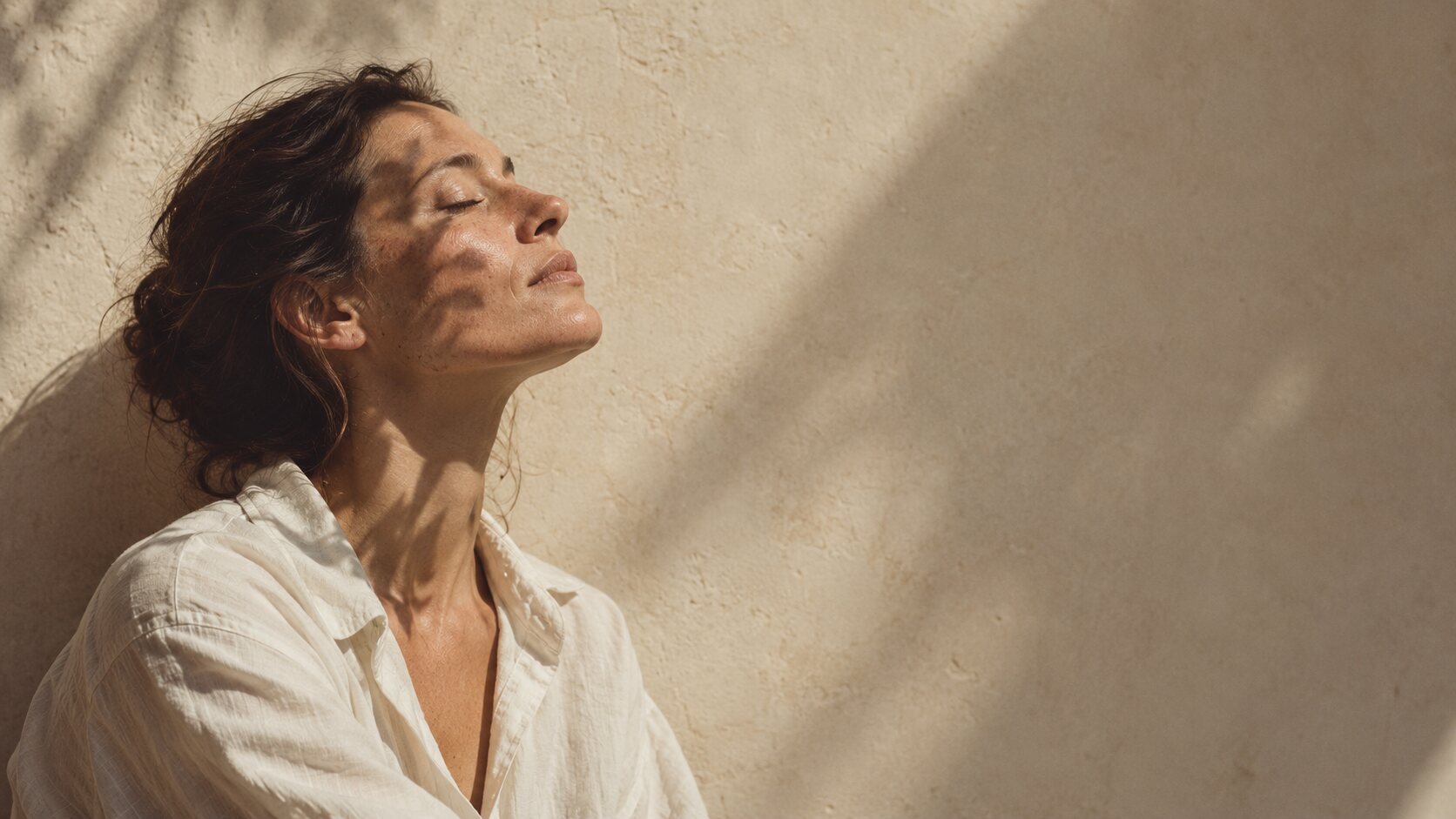 Frau mit geschlossenen Augen in der Sonne vor einer Putzwand